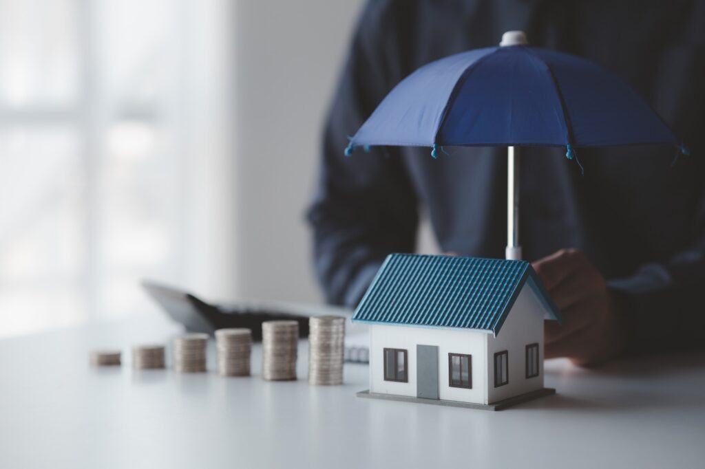 Individuals holding small umbrellas and model homes, housing insurance against impending loss and fi