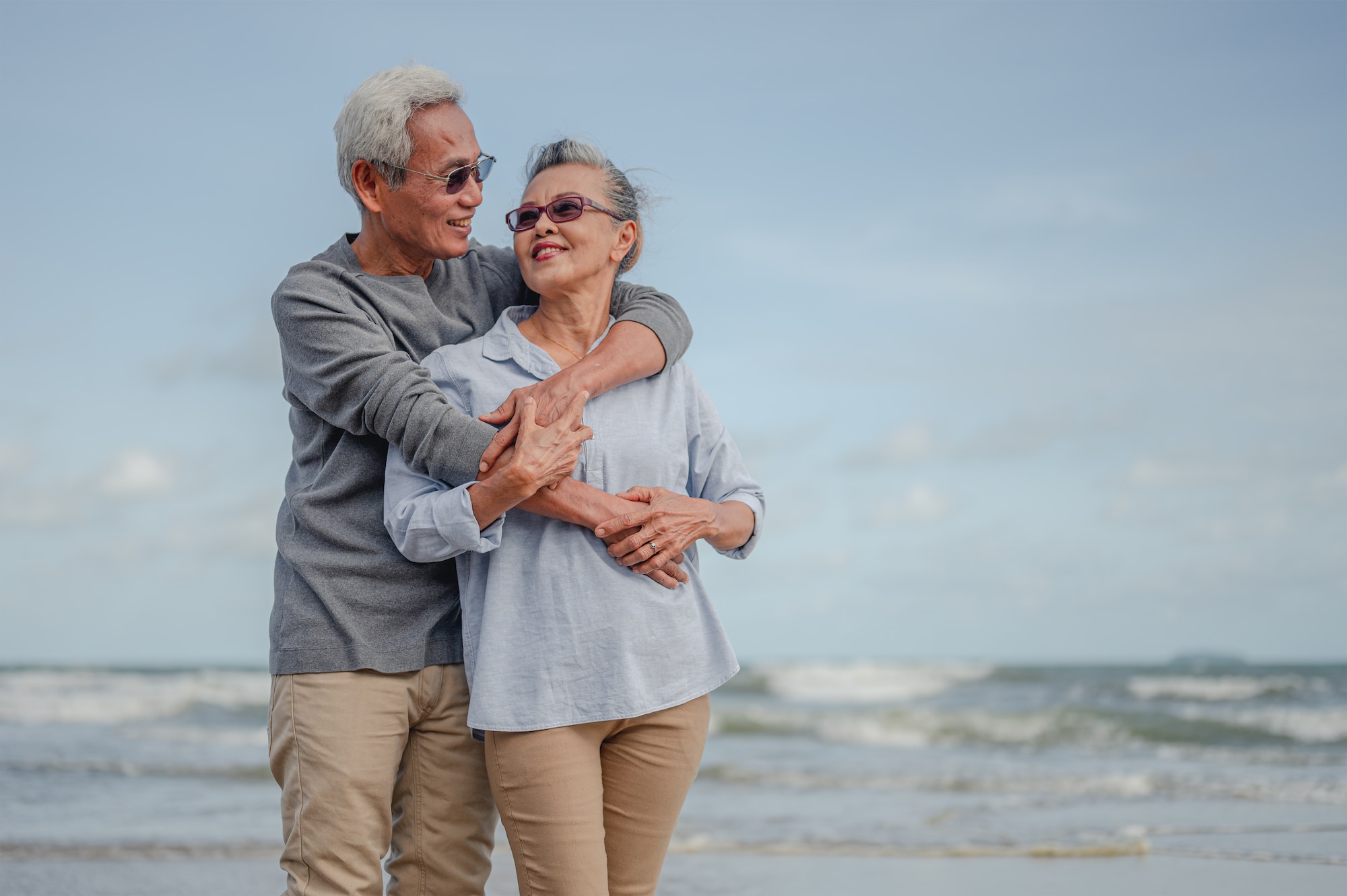 Senior couple embrace on the beach at not sunny day, plan life insurance with happy retirement.