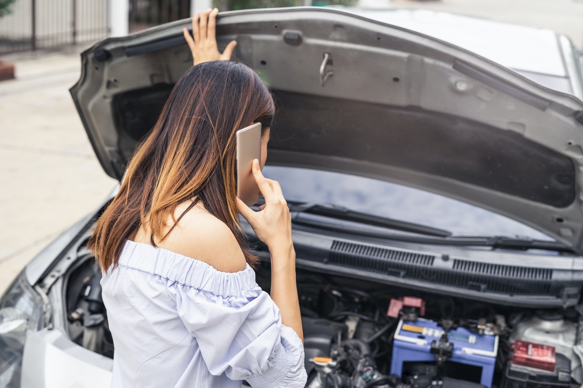 Young woman with broken down car using smartphone for assistance